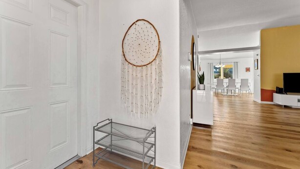 A modern living room with a wooden floor, a white door, and a dreamcatcher decoration.