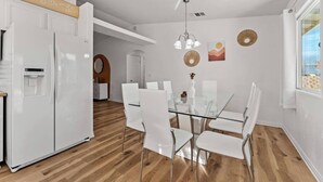 A modern kitchen with white appliances, a glass dining table, and a wooden floor.