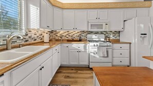 A modern kitchen with white cabinetry, a microwave, a stove, and a sink.