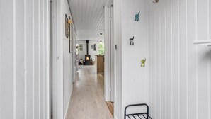 Un couloir étroit aux murs blancs et au plancher en bois, qui mène à une pièce dotée d’une cheminée et d’un banc en bois.