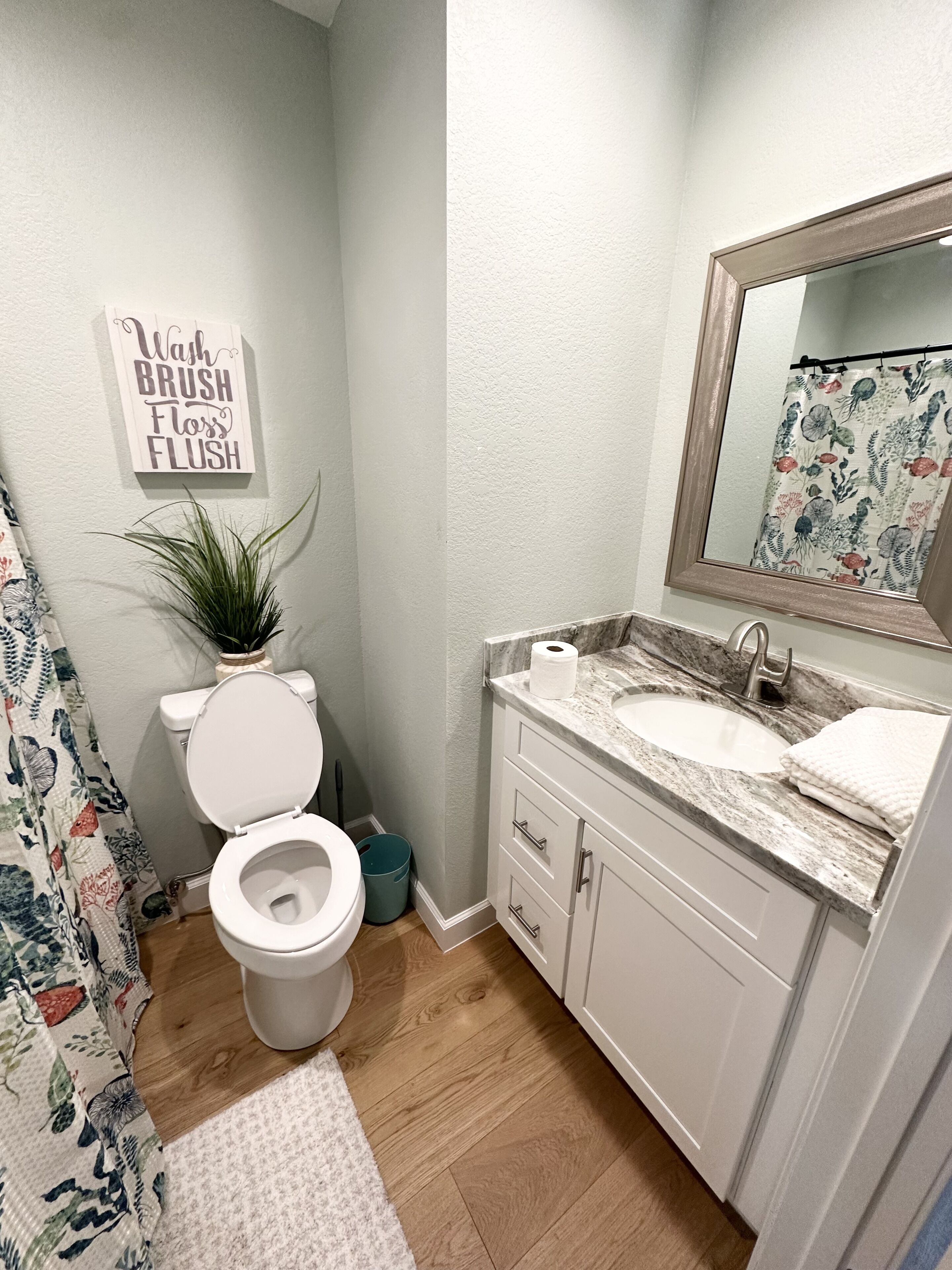 A bathroom with a toilet, sink, and mirror. There is a sign on the wall that says "Wash Brush Floss Flush."