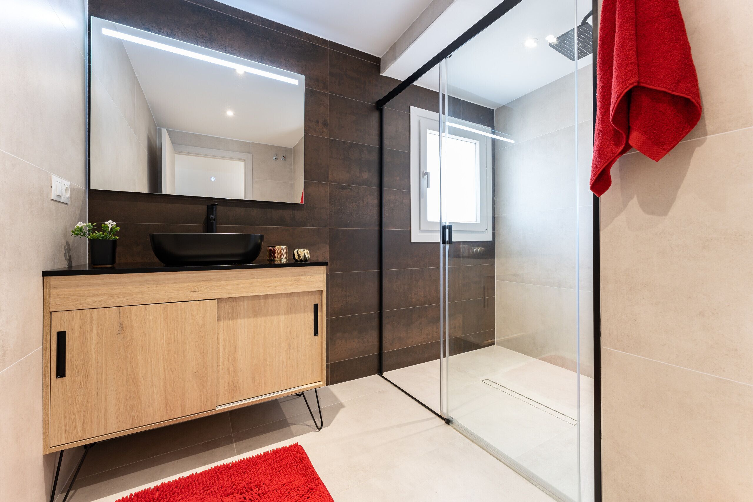 Een moderne badkamer met een houten wastafelmeubel, een zwarte wasbak en een douchecabine van glas.