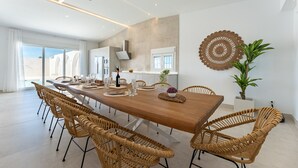 A modern dining area with a long wooden table, wicker chairs, and a large potted plant. - MalagaSuite Villa Nomada El Torcal (Antequera)