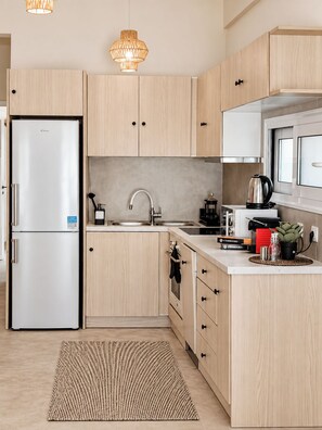 A modern kitchen with light wood cabinets, stainless steel appliances, a built-in oven, and a large window.