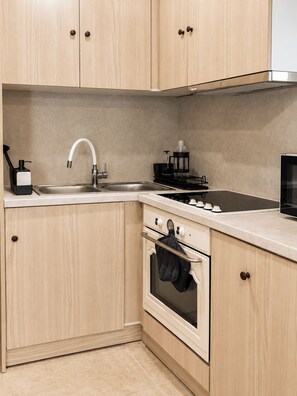 A kitchen with wooden cabinets, a stainless steel sink, a stove, and a microwave. - Bohemian Loft in Central Athens (Kypseli)