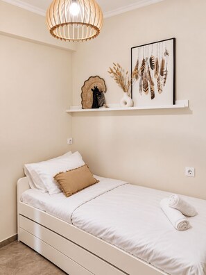 A minimalist bedroom with a single bed, a white nightstand, a wall-mounted shelf with decorative items, and a pendant light. - Bohemian Loft in Central Athens (Kypseli)