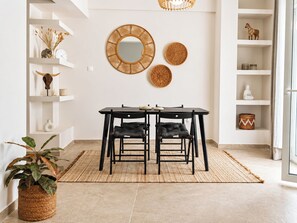 A dining area with a table and chairs, a woven rug, and shelves with decorative items.