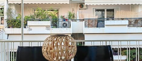 A balcony with wicker furniture, a potted plant, and a building with balconies in the background.