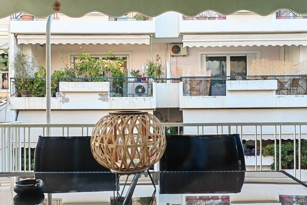 Ein Balkon mit Korbmöbeln, einem Blumentopf und einem Gebäude mit Balkonen im Hintergrund.