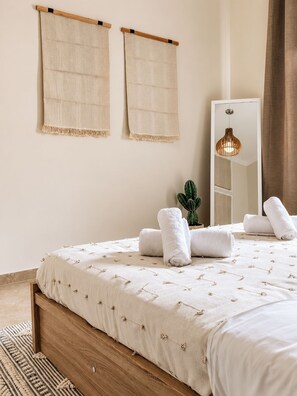 A bedroom with a bed, a mirror, a hanging towel, and a cactus plant.