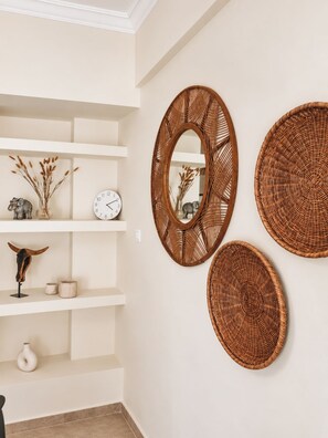 A room with a white wall, a clock, and three woven wall hangings.