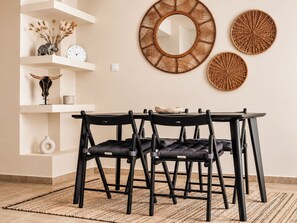 A dining area with a round table, black chairs, a woven wall hanging, and decorative items on shelves.