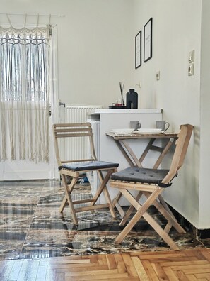 A compact room with a wooden floor, a small table, two foldable chairs, a radiator, and a door with a macramé curtain. - Funky Boho Kallithea Loft (Kallithea)