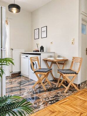 A compact kitchen with a dining area, featuring a white countertop, two foldable chairs, a hanging light fixture, and a radiator. - Funky Boho Kallithea Loft (Kallithea)
