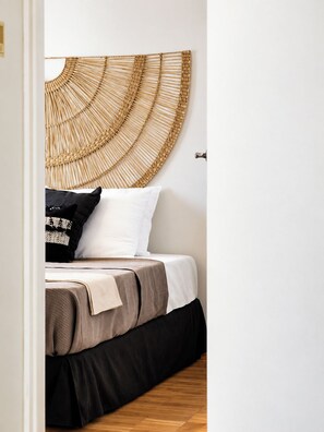 Una cama con cabecera circular trenzada, un almohadón blanco, un almohadón negro y una manta color beige.
