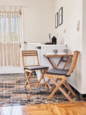 Una habitación con piso de madera, un radiador blanco, una mesita con una silla y una cortina de macramé.