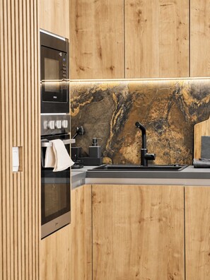 Una cocina moderna con armarios de madera, horno empotrado, microondas, pileta con grifo negro y salpicadero de mármol.