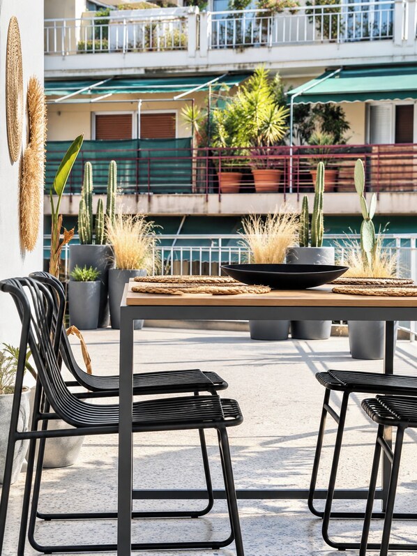 Un patio al aire libre con una mesa, sillas y plantas en macetas.