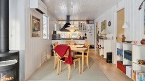A cozy kitchen with a dining area, featuring a wood-burning stove, white cabinetry, and a bookshelf with books. - 4 bedroom gorgeous home in Hornbæk (Hornbæk)