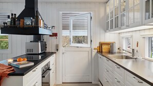 A compact kitchen with white cabinetry, a black range hood, and a window overlooking a garden. - 4 bedroom gorgeous home in Hornbæk (Hornbæk)