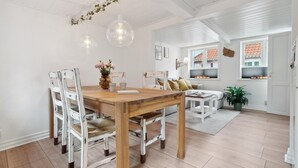Un coin repas avec une table en bois et des chaises peintes en blanc, un vase rempli de fleurs et des lampes suspendues.