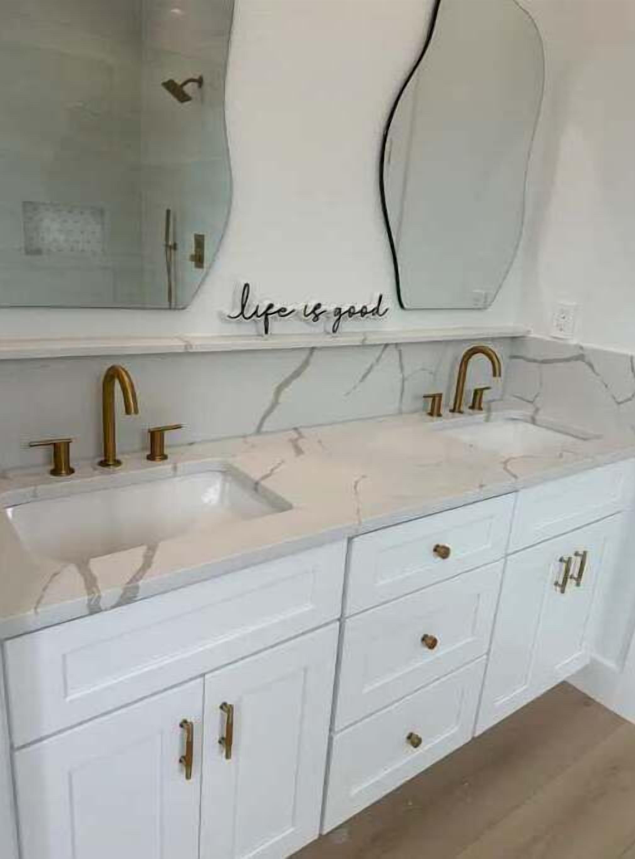 Un bagno con un mobile lavabo bianco, due lavandini, rubinetti dorati e uno specchio con la scritta 'life is good'.