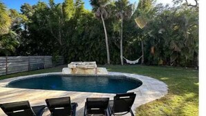 A swimming pool with a stone deck, surrounded by grass and palm trees. - Private Resort (Sarasota)