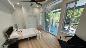 A bedroom with a bed, a desk, a chair, and a balcony with a view of greenery. - Private Resort (Sarasota)