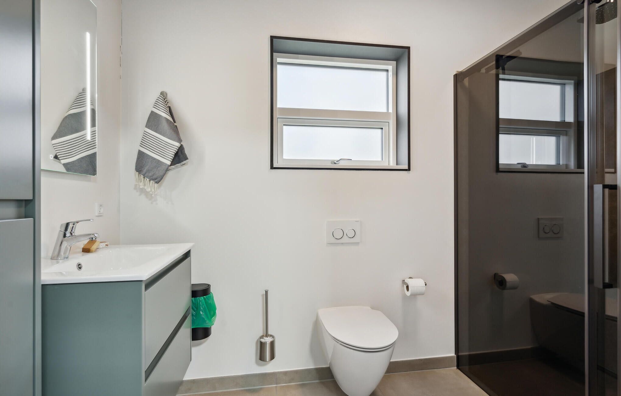 A modern bathroom with a toilet, sink, and two windows.