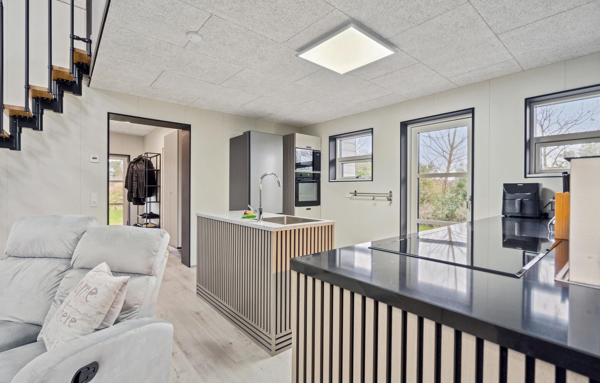 A modern kitchen with a central island, a built-in oven, and a window overlooking a garden.