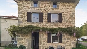 A two-story stone building with a flat roof, two windows with shutters, a door, and a small porch area with chairs. - 2 bedroom amazing home in Bas-en-Basset (Bas-en-Basset)