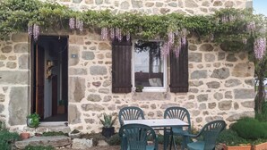 A stone building with a door and window, a table with chairs, and potted plants. - 2 bedroom amazing home in Bas-en-Basset (Bas-en-Basset)