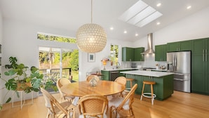 A modern kitchen with green cabinets, a stainless steel refrigerator, and a dining area with wicker chairs and a wooden table. - Pirates Perch I Whidbey I Hot Tub I King Bed (Freeland)