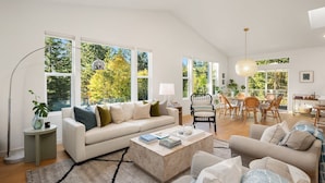 A spacious living room with a white sofa, a coffee table, and a dining area with wicker chairs. - Pirates Perch I Whidbey I Hot Tub I King Bed (Freeland)