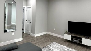 Una sala de estar moderna con un televisor de pantalla plana grande, un sofá gris, una mesa de centro y un espejo en la pared.