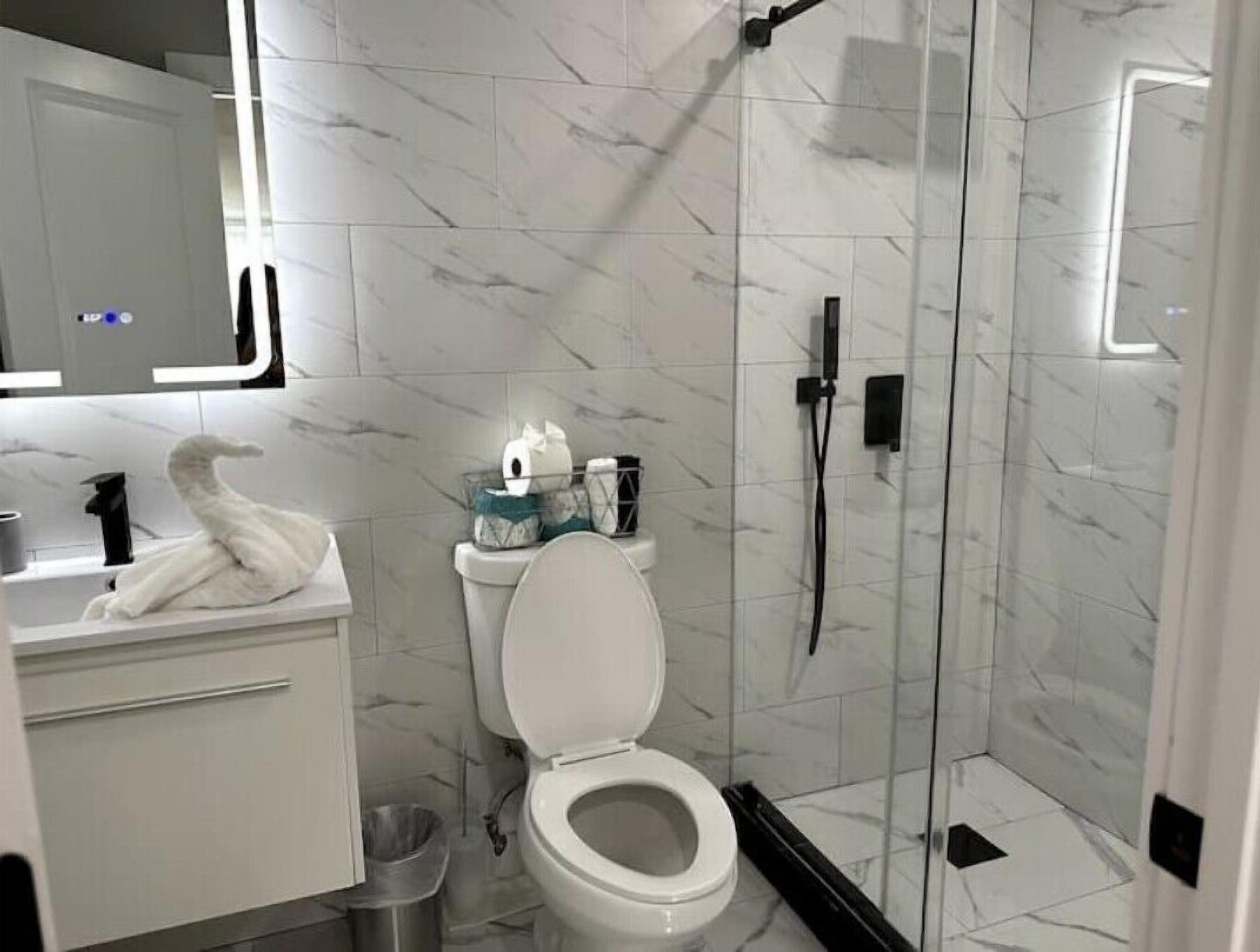 Une salle de bain moderne avec un sol en marbre, des toilettes blanches, une douche en verre et un meuble-lavabo doté d’un porte-serviettes.