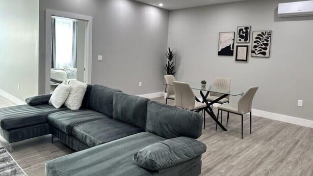 Una sala de estar moderna con un sofá modular, un comedor con una mesa de vidrio y sillas, y obras de arte en las paredes.