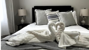 Un lit bien fait, avec un peignoir blanc et des serviettes disposées en forme de cœur.