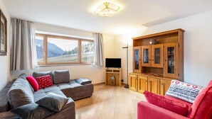 Uma sala de estar com um sofá, uma poltrona vermelha, um armário de madeira e uma televisão.