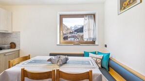 Quarto com cama, mesa com cadeiras, janela com vista para montanhas e um quadro na parede.