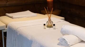 Une table de massage recouverte d’une serviette blanche, une bougie allumée et deux petits flacons d’huiles essentielles.