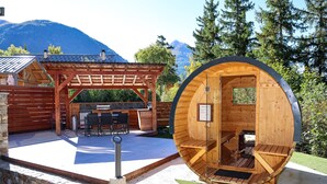Una cabana de fusta amb interior circular, una zona de pati amb una barbacoa i una paret de pedra.