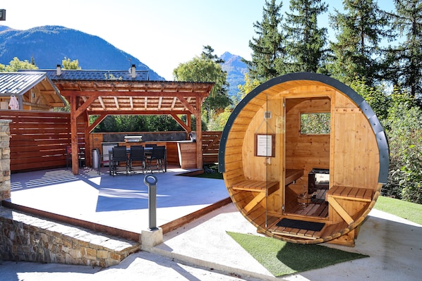 A wooden cabin with a circular interior, a patio area with a grill, and a stone wall.