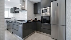 A modern kitchen with stainless steel appliances, a built-in oven, and a microwave. - Apartment "Refugio del Mar" with Sea View, Shared Pool & Wi-Fi (El puerto de santa maria)