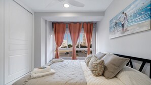 A bedroom with a large bed, a painting on the wall, and a window with curtains. - Apartment "Refugio del Mar" with Sea View, Shared Pool & Wi-Fi (El puerto de santa maria)