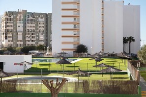 Een modern gebouw met meerdere balkons, een verzorgd gazon met parasols, en een heldere lucht.
