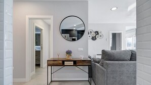 A modern living room with a grey sofa, a wooden desk with a mirror, and a kitchen visible through an open door. - Apartment "Refugio del Mar" with Sea View, Shared Pool & Wi-Fi (El puerto de santa maria)