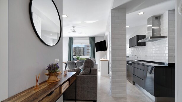 A modern kitchen with a built-in stove, a dining area with a wooden table and a gray sofa, and a large mirror on the wall. - Apartment "Refugio del Mar" with Sea View, Shared Pool & Wi-Fi (El puerto de santa maria)