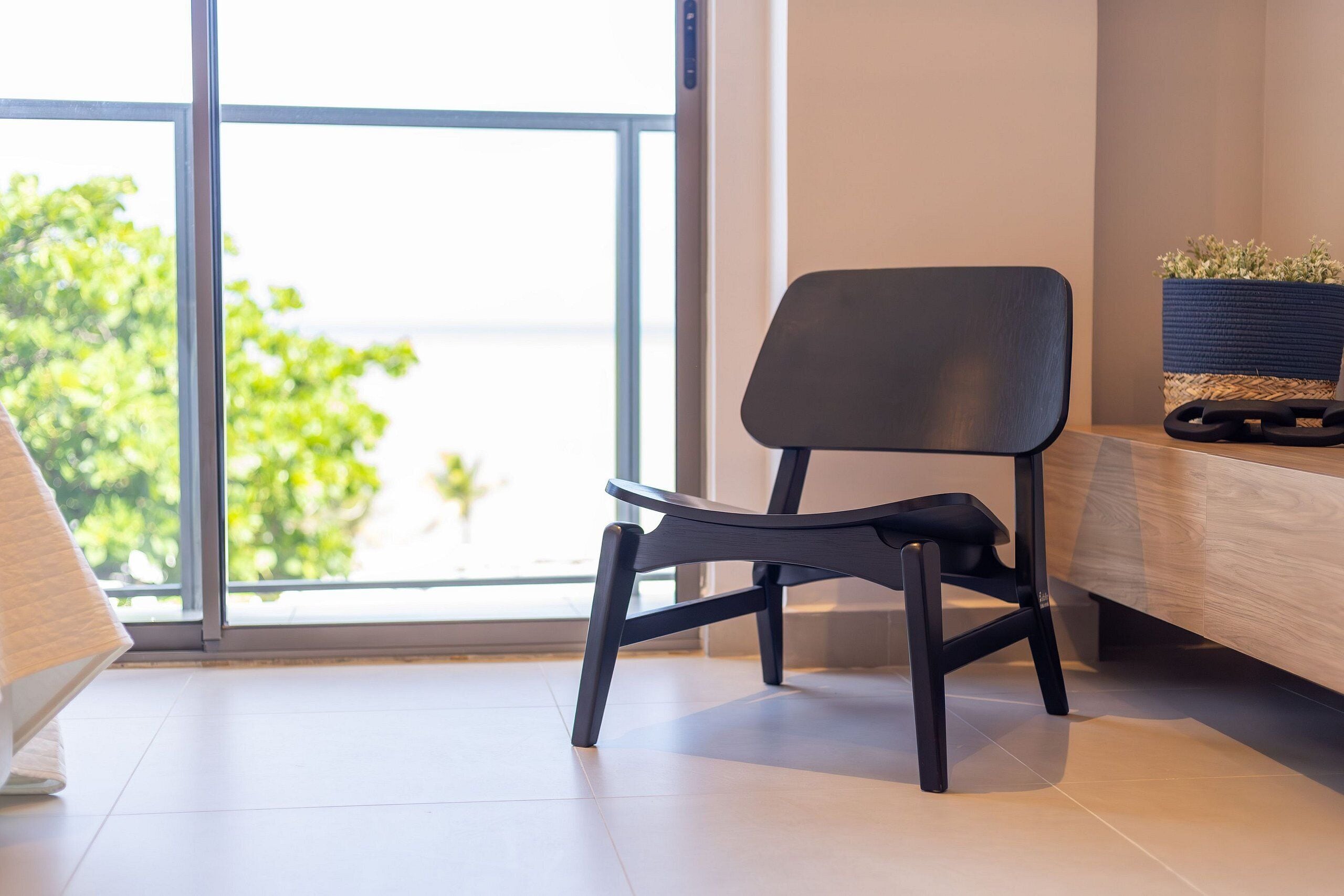 A modern office chair in a bright room with a large window, a wooden desk, and a woven basket with plants.