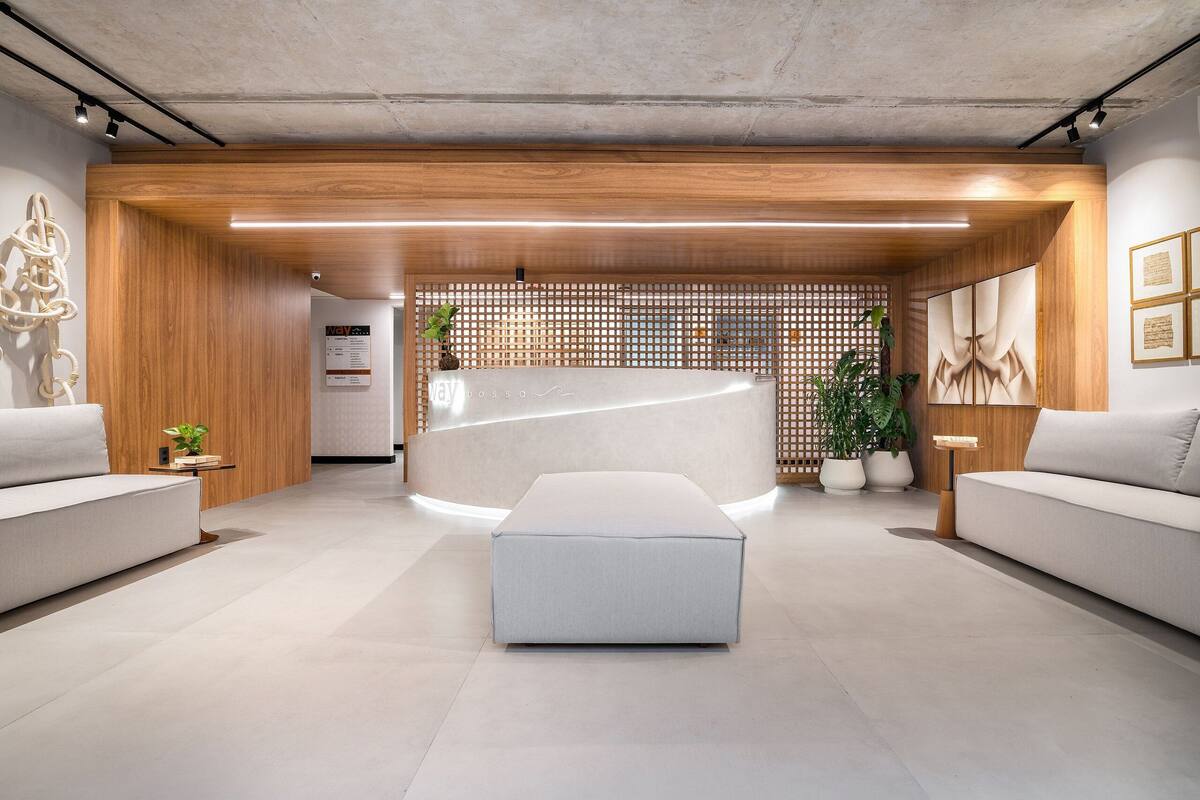 A modern reception area with a reception desk, two sofas, a large ottoman, wooden paneling, and a plant.